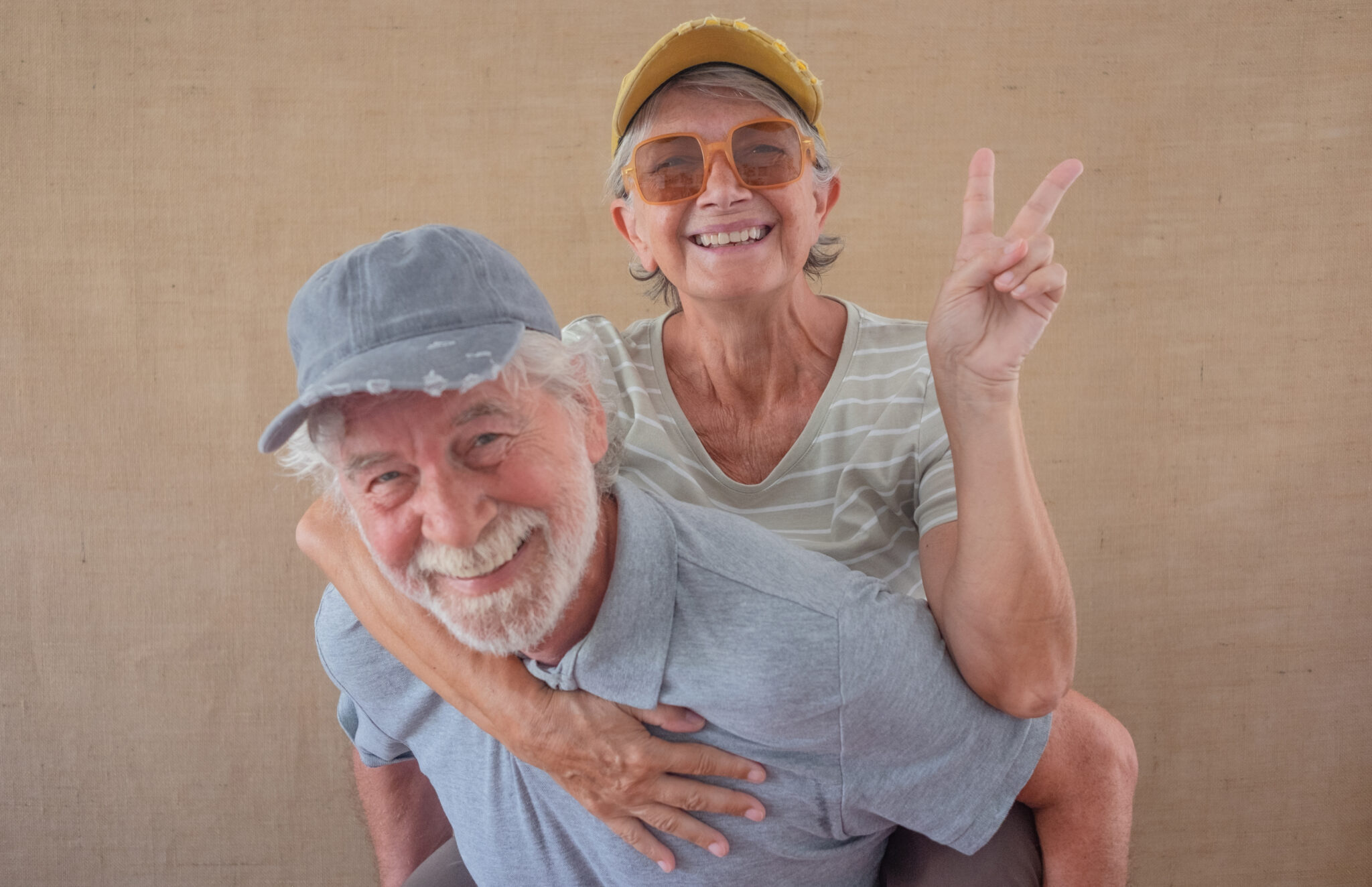 Image of cheerful senior couple having fun while man piggyback his wife, isolated over clear background